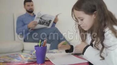 可爱的白种人女孩在VIP候车室画画的肖像，她的父亲在后台看报纸。 年轻人